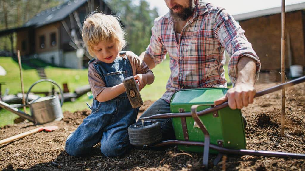 father with small son working outdoors in garden, sustainable lifestyle concept.