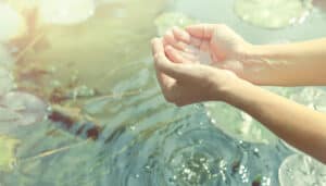 hands in cupped form getting water from a lake or fountain